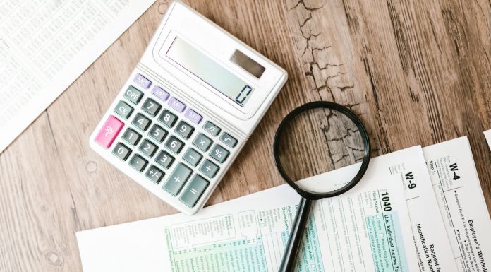 Tax forms laid out with a calculator and magnifying glass on a wooden surface, perfect for finance themes.