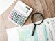 Tax forms laid out with a calculator and magnifying glass on a wooden surface, perfect for finance themes.