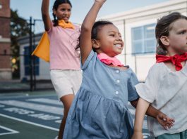 Three kids enjoying superhero play on a sunny outdoor court.