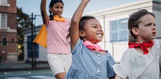 Three kids enjoying superhero play on a sunny outdoor court.