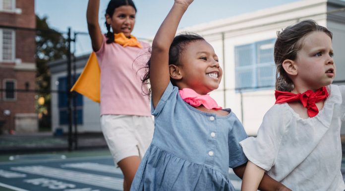 Three kids enjoying superhero play on a sunny outdoor court.