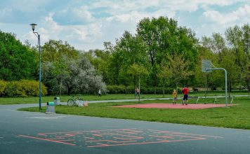 A father and child enjoy playing basketball on an outdoor court in a green, tranquil park setting.
