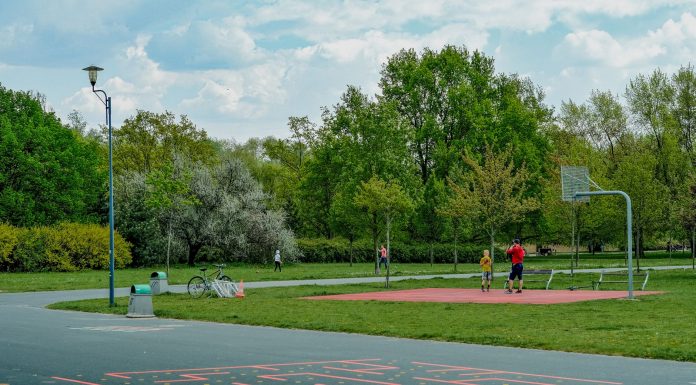 A father and child enjoy playing basketball on an outdoor court in a green, tranquil park setting.