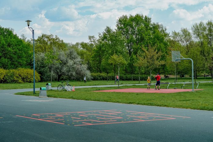A father and child enjoy playing basketball on an outdoor court in a green, tranquil park setting.