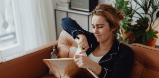 Jersey City resident blasts 15.5% tax hike, calls budget ‘irresponsible’ Woman in pajamas tearing paper on a sofa, expressing frustration. Indoors setting with laptop nearby.