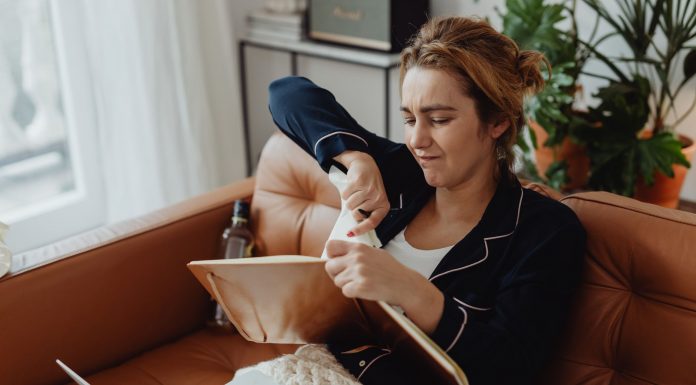 Woman in pajamas tearing paper on a sofa, expressing frustration. Indoors setting with laptop nearby.