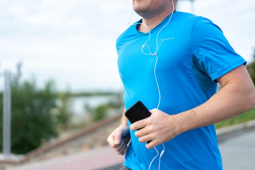Close-up of a man jogging outdoors holding a smartphone wearing earphones.