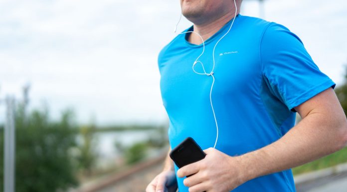 Close-up of a man jogging outdoors holding a smartphone wearing earphones.