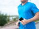 Close-up of a man jogging outdoors holding a smartphone wearing earphones.