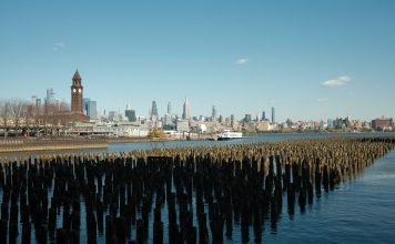 Cómo Sacar la Licencia de Conducir en NJ desde Bayonne: Guía Completa 2026 Scenic view of New York City skyline from Hoboken waterfront with wooden piers in the foreground.