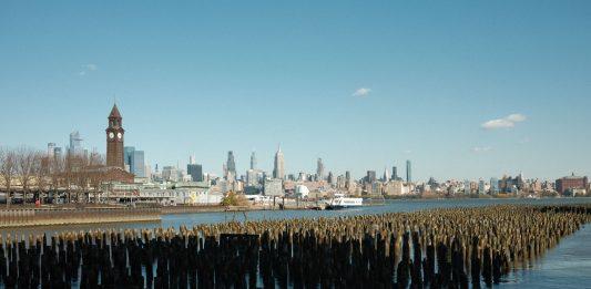 Cómo Sacar la Licencia de Conducir en NJ desde Bayonne: Guía Completa 2026 Scenic view of New York City skyline from Hoboken waterfront with wooden piers in the foreground.