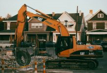 ÚLTIMA HORA: Aprueban demolición del 99¢ Dream Store en Newark Ave Excavator working in a suburban neighborhood construction site, with residential houses in the background.