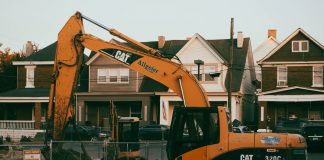 Excavator working in a suburban neighborhood construction site, with residential houses in the background.