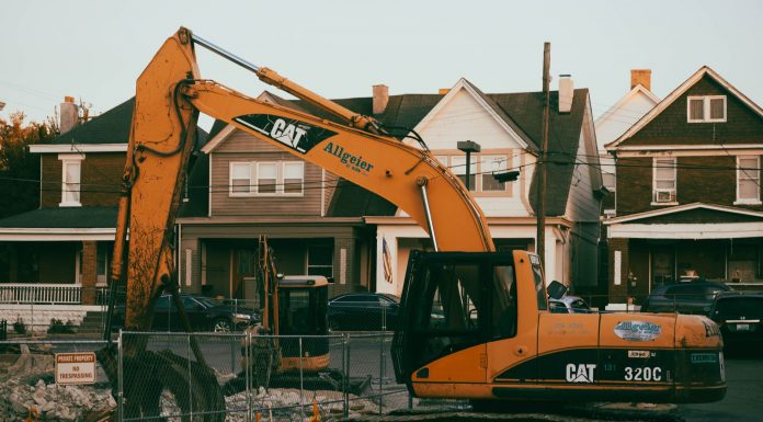 Excavator working in a suburban neighborhood construction site, with residential houses in the background.