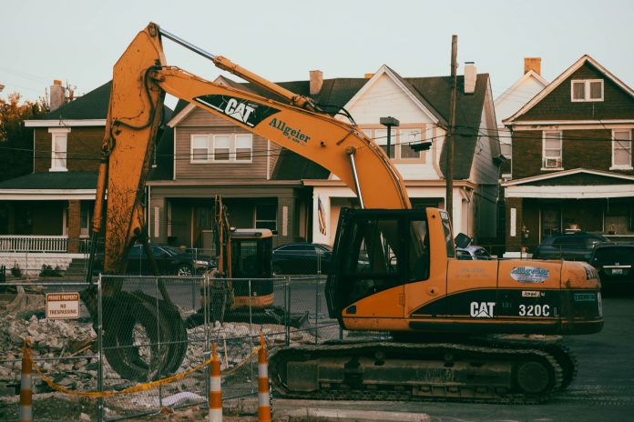 ltima-hora-aprueban-demolici-n-del-99-dream-store Excavator working in a suburban neighborhood construction site, with residential houses in the background.