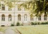 A vintage building with arched windows and greenery in a peaceful setting.