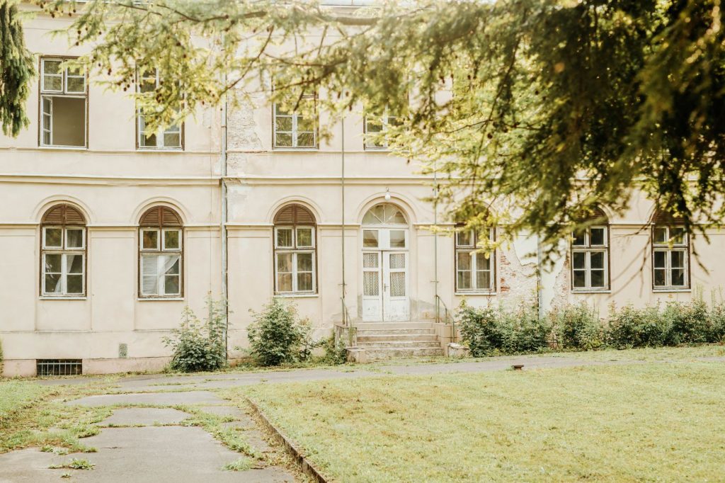 A vintage building with arched windows and greenery in a peaceful setting.