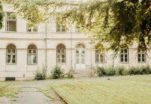 A vintage building with arched windows and greenery in a peaceful setting.