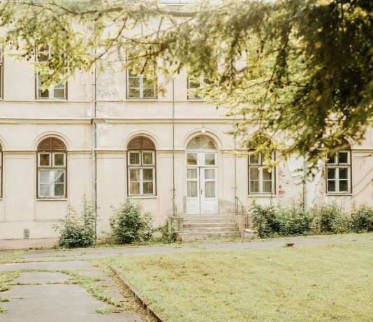A vintage building with arched windows and greenery in a peaceful setting.