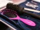 Close-up of pink and black hairbrushes on a towel in a salon setting.