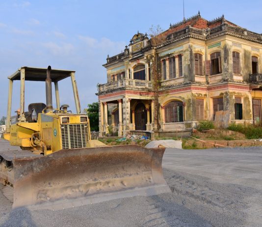 Historic building with a bulldozer outside on a construction site, under a clear sky.