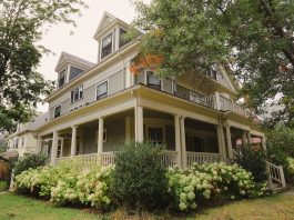 Charming traditional house with a wraparound porch, surrounded by lush garden.
