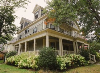 Charming traditional house with a wraparound porch, surrounded by lush garden.
