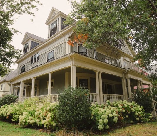 Charming traditional house with a wraparound porch, surrounded by lush garden.