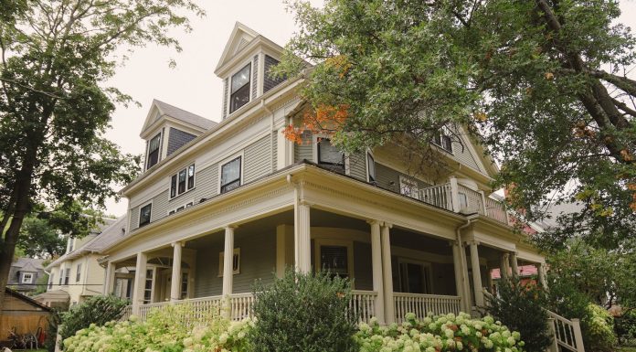 Charming traditional house with a wraparound porch, surrounded by lush garden.