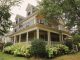 Charming traditional house with a wraparound porch, surrounded by lush garden.