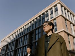 Two stylish women in coats in a business district with modern architecture.