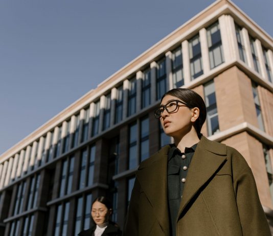 Two stylish women in coats in a business district with modern architecture.
