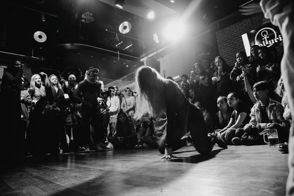 Dynamic black and white shot of a dancer performing to an enthralled crowd in a lively venue.