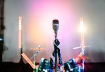 Retro microphone on a stage with colorful lights and a drum set, perfect for music themes.