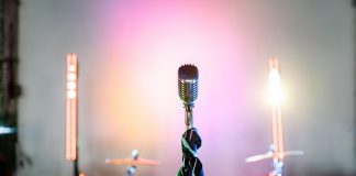 Retro microphone on a stage with colorful lights and a drum set, perfect for music themes.