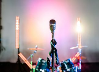 ÚLTIMA HORA: Suit & Mai Tai animará concierto en Bayonne Retro microphone on a stage with colorful lights and a drum set, perfect for music themes.