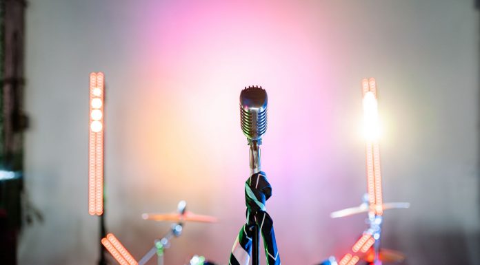 Retro microphone on a stage with colorful lights and a drum set, perfect for music themes.