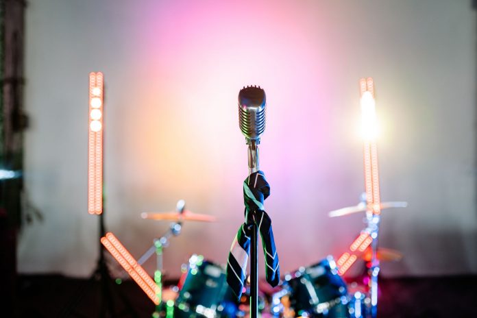ltima-hora-suit-mai-tai-animar-concierto-en-bayon Retro microphone on a stage with colorful lights and a drum set, perfect for music themes.