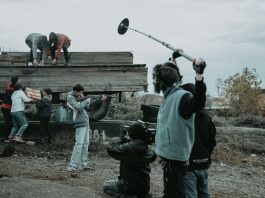 Film crew working outdoors, capturing scenes with camera and boom mic.