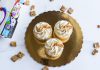 Top view of three cinnamon toast cupcakes with frosting on a golden tray, surrounded by cereal.