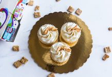 Top view of three cinnamon toast cupcakes with frosting on a golden tray, surrounded by cereal.