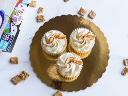 Top view of three cinnamon toast cupcakes with frosting on a golden tray, surrounded by cereal.