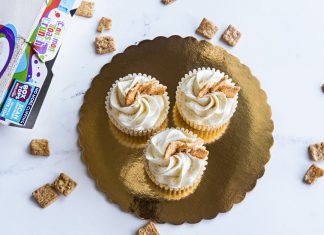 Top view of three cinnamon toast cupcakes with frosting on a golden tray, surrounded by cereal.
