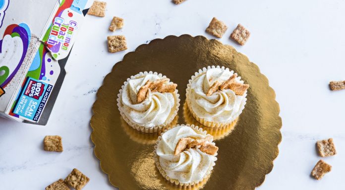Top view of three cinnamon toast cupcakes with frosting on a golden tray, surrounded by cereal.