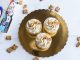Top view of three cinnamon toast cupcakes with frosting on a golden tray, surrounded by cereal.