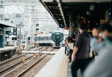 A train arriving at a bustling Japanese station filled with waiting passengers.