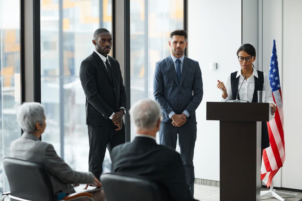 Professional speakers presenting at a conference in a modern room with glass windows.