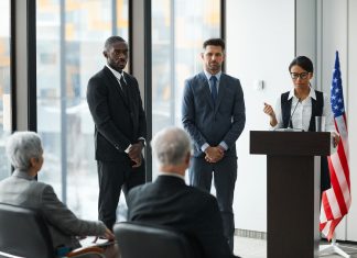 Professional speakers presenting at a conference in a modern room with glass windows.