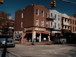 Street view of Joe's Pizza on a sunny day in Brooklyn, showcasing the lively urban atmosphere.