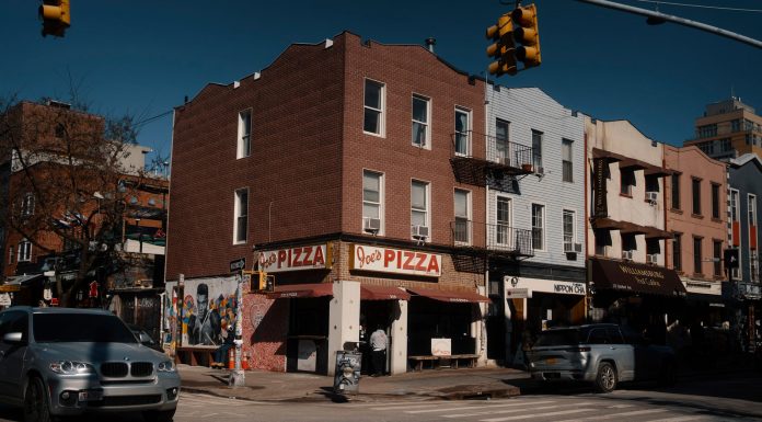 Street view of Joe's Pizza on a sunny day in Brooklyn, showcasing the lively urban atmosphere.